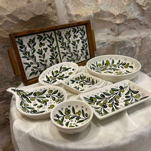 Puede incluir: Conjunto de fuentes de cerámica blanca con diseño de rama de olivo verde. El conjunto incluye una bandeja rectangular, cuencos ovalados y varios platos pequeños. El patrón de la rama de olivo se repite.