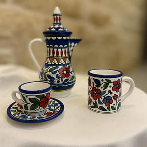 May include: A ceramic coffee set featuring a blue and white coffee pot, a cup and saucer, and a mug. The set is decorated with red and blue floral patterns. The coffee pot is approximately 20 cm tall.