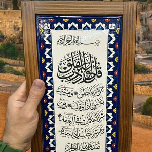 Puede incluir: Una obra de arte islámica enmarcada con caligrafía negra sobre fondo blanco. El marco de madera rodea un borde con diseño azul y blanco. Una pieza decorativa.