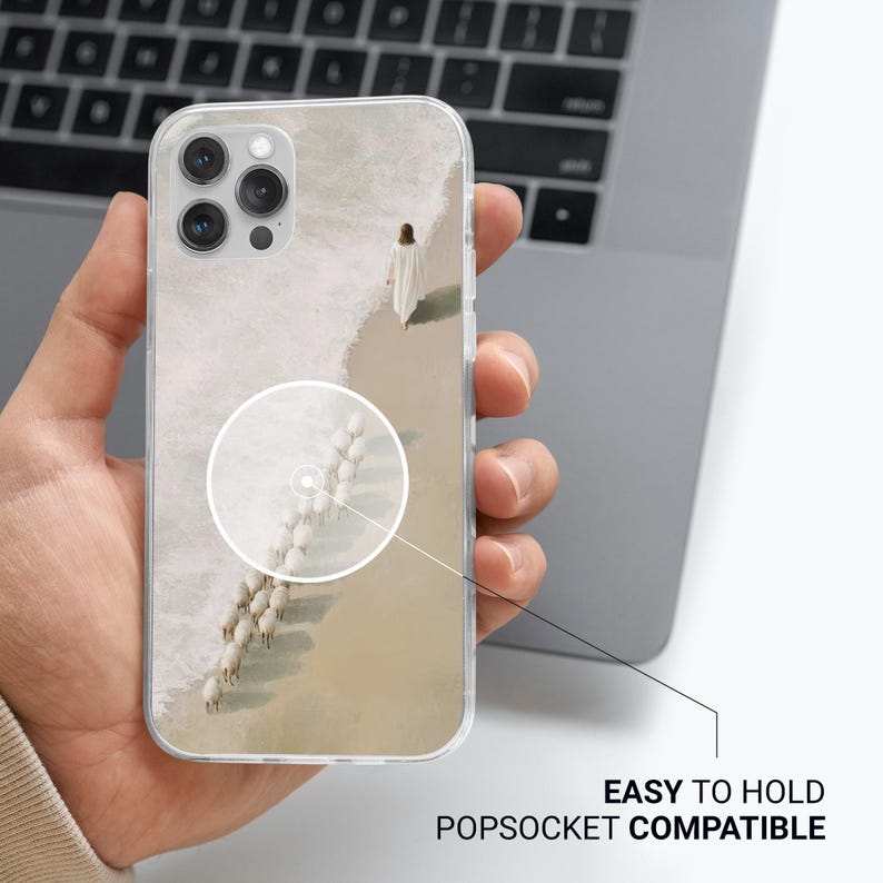 May include: Clear phone case featuring a serene beach scene with a person in white walking along the shore, followed by a flock of sheep. The case is labeled "EASY TO HOLD POPSOCKET COMPATIBLE".