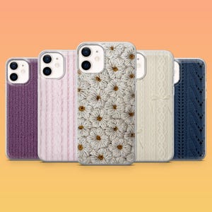 May include: A collection of five phone cases with various textured designs. The cases include a purple knit, a light pink cable knit, a white daisy pattern, a cream-colored knit with a bow, and a navy blue knit. The cases are displayed against an orange background.