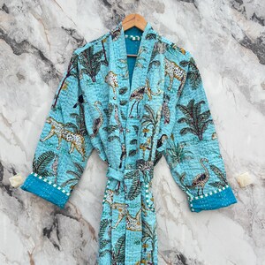 May include: A light blue robe with a jungle animal print, including leopards, birds, and palm trees. The robe has a matching belt and contrasting blue cuffs. The robe is hanging on a wooden hanger.