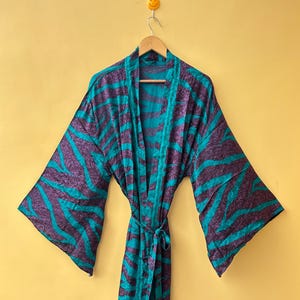 May include: A long-length robe featuring a vibrant teal and dark purple zebra-inspired animal print pattern. The garment includes wide, loose-fitting sleeves, an open front design, and a matching fabric tie belt at the waist for closure.