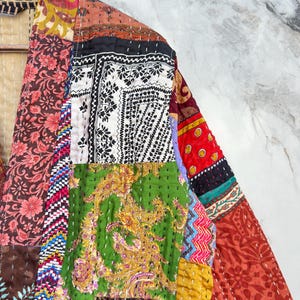 Könnte beinhalten: Patchwork-Jacke mit einer Vielzahl farbenfroher Stoffmuster, darunter Blumen-, Paisley- und geometrische Designs. Die Jacke besteht aus mehreren Stoffstücken, die zusammengenäht wurden, wodurch ein einzigartiger und künstlerischer Look entsteht. Die Jacke hängt an einem Holzbügel.