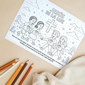 Puede incluir: Una p&aacute;gina para colorear en blanco y negro con cuatro ni&ntilde;os tomados de la mano, con el texto "JES&Uacute;S ES LA LUZ" y una cruz. Los ni&ntilde;os visten camisetas con una cruz. L&aacute;pices de colores en tonos marrones y amarillos en primer plano.