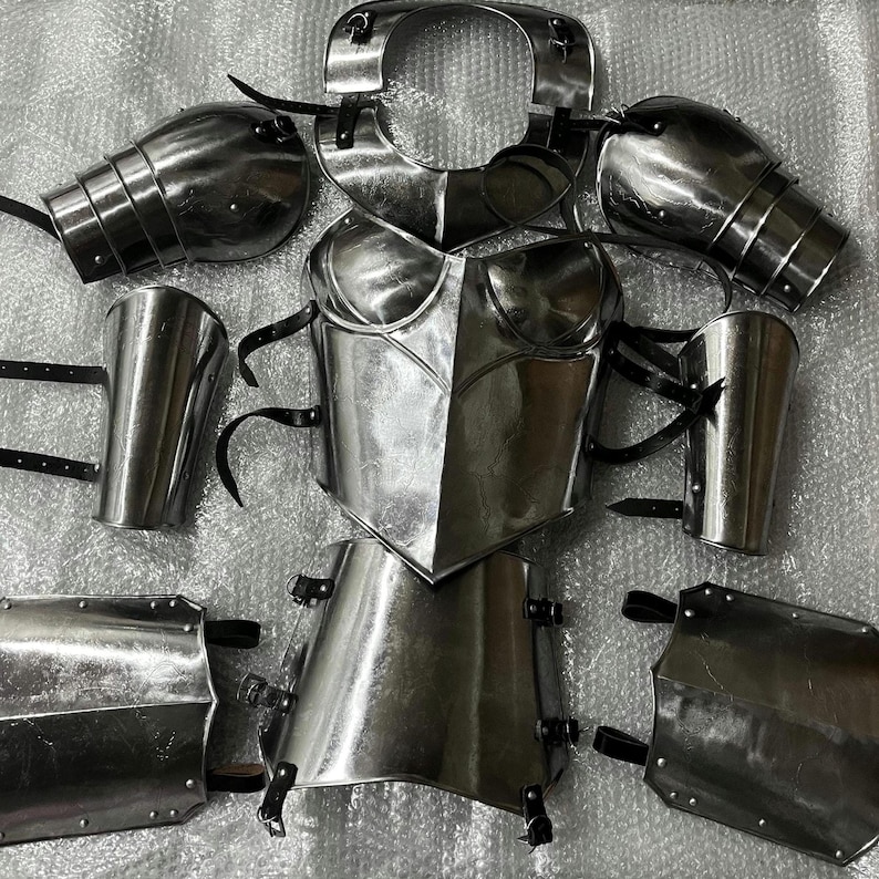 May include: A polished steel suit of armour set including a breastplate, gorget, pauldrons, vambraces, and greaves. Each piece features a reflective metallic finish and is equipped with black leather straps and metal buckles for secure fastening..