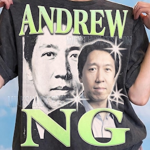 May include: A charcoal gray t-shirt featuring a large graphic print of Andrew Ng. The design includes the name ANDREW NG in large light green letters, two portraits of the individual, and several white starburst accents. The shirt has a faded wash.