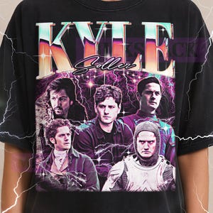 May include: Black t-shirt featuring a graphic design with the name "KYLE" in large, colorful letters, and the name "Soller" in script. The design includes images of several men. The Milkshake logo is at the top.