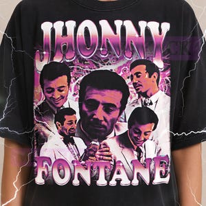 May include: Black t-shirt featuring a graphic of the name "JHONNY" above a collage of images of a man in a suit. The word "FONTANE" is below the images. The Milkshake logo is at the top.