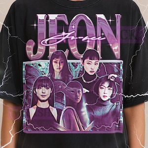 May include: Black t-shirt featuring a graphic design with the word "JEON" in large, purple letters above a collage of five people. The Milkshake logo is visible at the top.