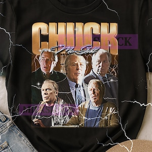 May include: Black t-shirt with a retro graphic design. The design features the text "CHUCK McGILL" in gold, with a collage of images of the actor. The design has a vintage aesthetic with lightning bolt accents.
