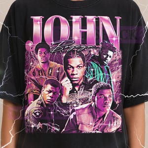 May include: Black t-shirt featuring a graphic of John Boyega and the text "JOHN Boyega" in a retro style. The design includes multiple images of the actor with a purple and pink color scheme. The Milkshake logo is at the top.