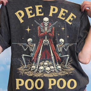 May include: Dark gray t-shirt with a graphic featuring a skeleton in a red coat holding two pistols, flanked by two skeletons with rifles. The text "PEE PEE" and "POO POO" are in gold, with the text "Comfort Colors: Pepper" at the bottom.