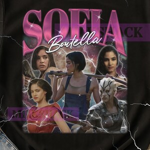Könnte beinhalten: Schwarzes T-Shirt mit einem Retro-Grafikdesign von Sofia Boutella. Das Design umfasst ihren Namen in einem rosa Farbverlauf, Bilder von ihr in verschiedenen Rollen und einen kosmischen Hintergrund mit Blitzeffekten.