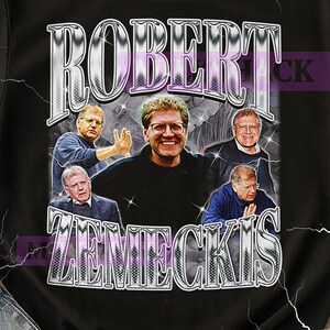 Op de afbeelding: Zwart T-shirt met een retro graphic van Robert Zemeckis, zijn naam in een zilveren, vintage lettertype. Het ontwerp bevat meerdere afbeeldingen van Zemeckis. Het shirt heeft een klassieke ronde hals.