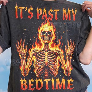 May include: Dark grey t-shirt with a flaming skeleton graphic. The text "IT'S PAST MY BEDTIME" is in fiery orange letters. The shirt also features the text "MILKSHACK.ETSY.COM" and "Comfort Colors : Pepper".