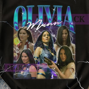 Op de afbeelding: Zwart t-shirt met een retro-stijl afbeelding van Olivia Munn. Het ontwerp bevat meerdere afbeeldingen van de actrice, de naam "OLIVIA MUNN", bliksemaccenten en een paarse achtergrond.
