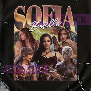 Könnte beinhalten: Schwarzes T-Shirt mit einem Grafikdesign mit dem Namen "SOFIA Boutella" in Gold und Lila. Das Design enthält mehrere Bilder einer Frau, vor einem Weltraumhintergrund mit Blitzen.