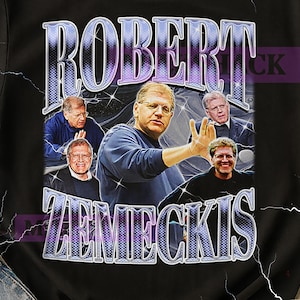 Op de afbeelding: Zwart T-shirt met een grafisch ontwerp. Het ontwerp toont de naam "ROBERT ZEMECKIS" in een paarse en zilveren lettertype en meerdere afbeeldingen van een man. Ronde hals.