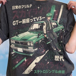 Puede incluir: Camiseta color pimienta con un gráfico de coche verde vintage y un personaje de estilo anime japonés. El diseño incluye texto japonés y detalles de estilo de placa de circuito. Diseñado por MILKSHACK.