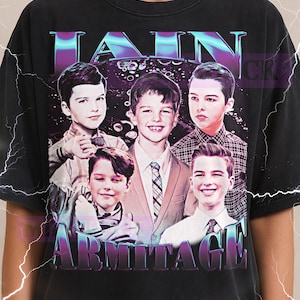May include: Black t-shirt featuring a graphic of five young men with the text "Young Sheldon Armitage" in a purple and blue gradient. The Milkshake logo is at the top.