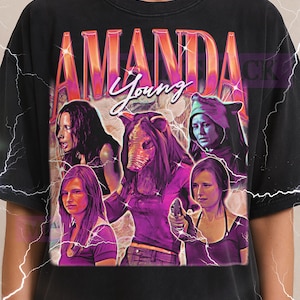 Può includere: T-shirt nero con un design grafico con la scritta "AMANDA Young" in stile retrò. Il design include immagini di diverse donne. Il logo Milkshake è in alto.