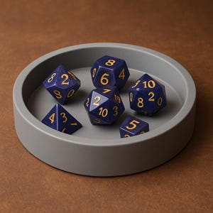 May include: A set of six navy blue polyhedral dice with gold numbering, resting in a gray circular tray. The dice are various shapes, including a four-sided die, a six-sided die, an eight-sided die, a ten-sided die, a twelve-sided die, and a twenty-sided die.