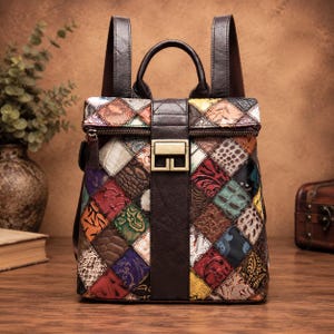 May include: A backpack featuring a multi-colored patchwork design with various embossed textures. The bag has a dark brown vertical center strap with a rectangular gold-tone metal buckle, a top handle, and two shoulder straps attached to the back.