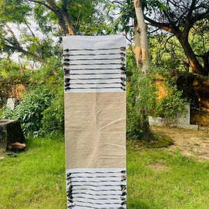 May include: A rectangular runner rug featuring a central solid tan section flanked by white ends. The white sections are decorated with horizontal black stripes and finished with small black tassels along the edges of the fabric.