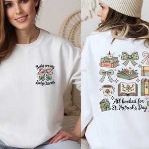 May include: White sweatshirt with a St. Patrick's Day theme. The front features text that reads "Books are my Lucky Charms" with a bow and shamrocks. The back has illustrations of books, bows, and a coffee mug with the text "All booked for St. Patrick's Day."