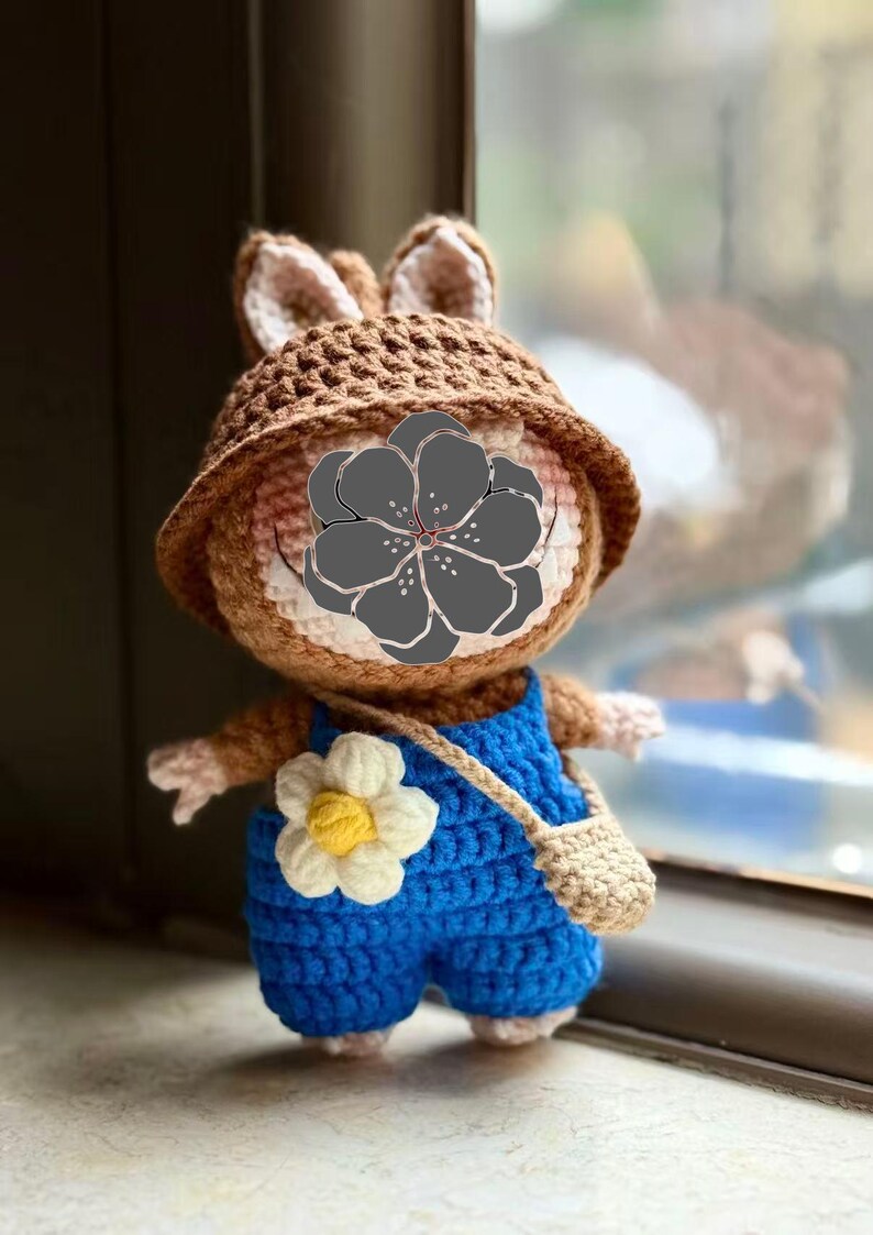 Peut inclure: Poup&eacute;e lapin au crochet faite &agrave; la main, portant un chapeau marron et une salopette bleue. La poup&eacute;e a une fleur blanche et jaune sur la salopette et un petit sac beige. Le lapin a une apparence mignonne et amicale.