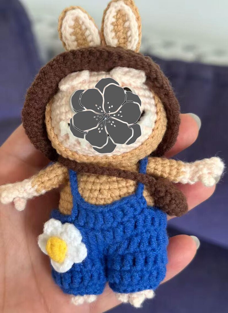 Peut inclure: Poup&eacute;e au crochet faite &agrave; la main repr&eacute;sentant un personnage de lapin. La poup&eacute;e porte une salopette bleue avec une fleur blanche et jaune. Elle a un chapeau marron et un petit sac marron. La poup&eacute;e est faite de fil beige, marron et blanc.