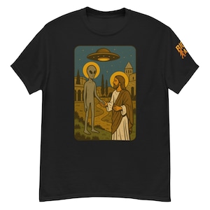 May include: Black t-shirt featuring a graphic of an alien and Jesus shaking hands under a UFO. The design is set against a backdrop of a landscape with buildings and trees. The shirt has a crew neck and short sleeves.
