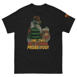 May include: Black t-shirt with a cartoon alien wearing a brown hat and a green and black striped sweater, holding medical tools. The text "ONE, TWO, HE'S GONNA PROBE YOU!" is printed in yellow and orange.
