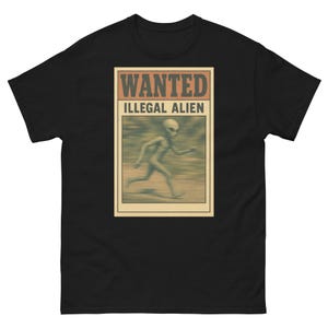 May include: Black t-shirt featuring a vintage-style "WANTED: ILLEGAL ALIEN" poster graphic. The poster shows a running alien figure in shades of green and brown. The text is in a bold, distressed font.