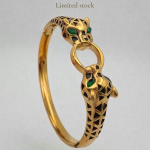 May include: Gold-coloured bracelet with two jaguar heads, green gemstone eyes, and black geometric patterns. The hinged bracelet has the text "Limited stock".