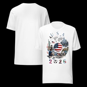 Pu&ograve; includere: T-shirt bianca con un design grafico. Il design include il testo "USA 2026", una bandiera americana, un pallone da calcio e illustrazioni di monumenti come la Statua della Libert&agrave; e l'insegna di Hollywood.