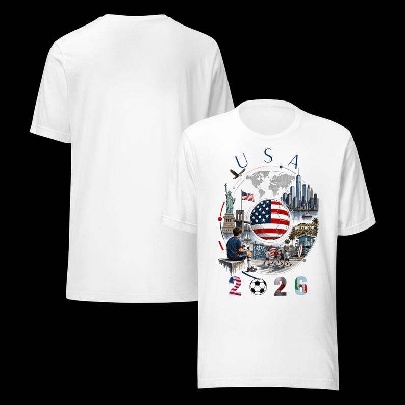 Pu&ograve; includere: T-shirt bianca con un design grafico. Il design include il testo "USA 2026", una bandiera americana, un pallone da calcio e illustrazioni di monumenti come la Statua della Libert&agrave; e l'insegna di Hollywood.
