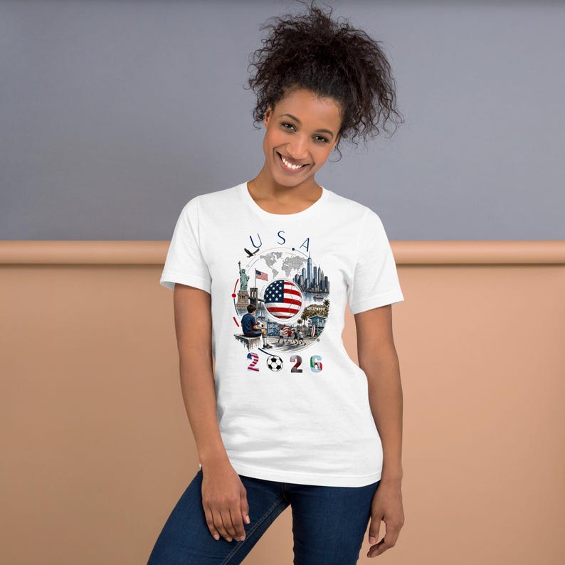 Pu&ograve; includere: T-shirt bianca con un design grafico colorato. Il design include la scritta "USA", la bandiera americana, un pallone da calcio e il numero "2026". La maglietta &egrave; realizzata in un materiale morbido.