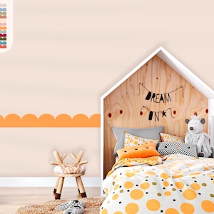 May include: A wall decal featuring a scalloped border in orange, applied to a light beige wall. The room includes a house-shaped wooden bed frame with bedding in orange and white polka dots, a plush toy, and a small wooden stool with antlers.