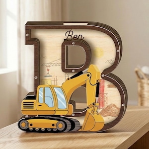 Può includere: Una banca a forma di lettera "B" in legno con un tema di costruzione. La banca presenta un giocattolo escavatore giallo di fronte a uno sfondo marrone chiaro con illustrazioni di cantiere. Il nome "Ben" è scritto in corsivo sulla banca.