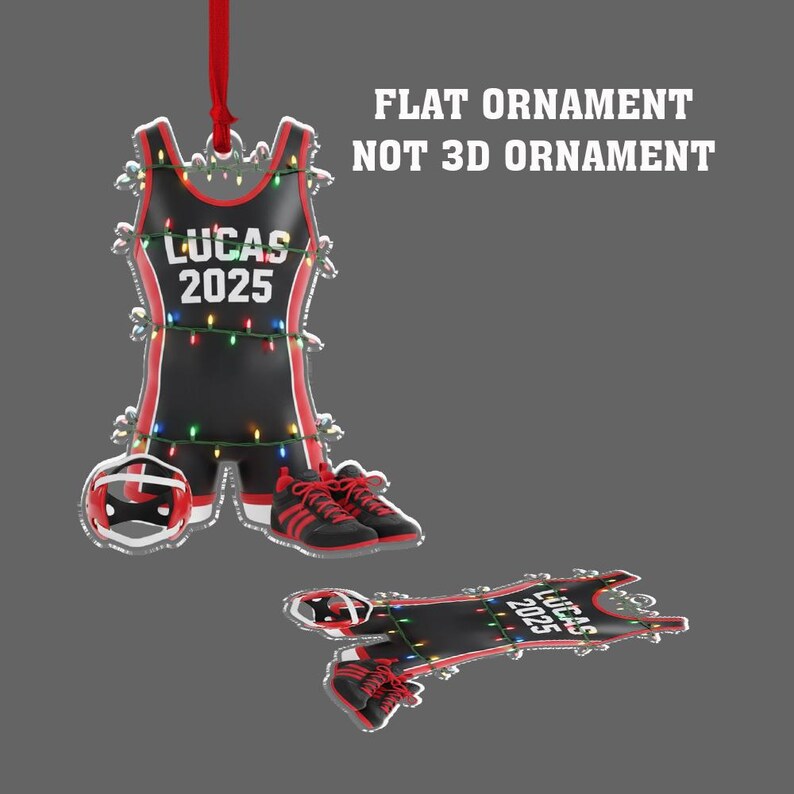 May include: A flat ornament shaped like a wrestling singlet, shoes, and headgear. The black singlet has red trim and the name "LUCAS 2025" printed on it. The ornament is decorated with small, colourful lights and a red ribbon.