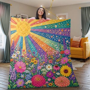 May include: A colorful blanket featuring a vibrant design of a sunburst with rainbow rays and a field of flowers. The blanket showcases a variety of flowers in shades of pink, yellow, purple, and white. The design is detailed and eye-catching.