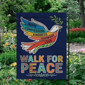 May include: A navy blue garden flag features a colorful dove carrying an olive branch. The dove's wings display the words "HOPE, COMPASSION, KINDNESS, HARMONY, LOVE." The flag reads "WALK FOR PEACE" in vibrant letters.