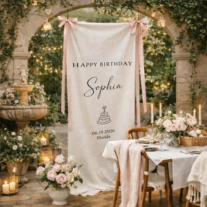 May include: A beige banner with the text "HAPPY BIRTHDAY Sophia" and a cake illustration. Pink ribbons hang from the top. The scene includes a table set for a party, a fountain, and floral arrangements.