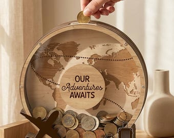 May include: A wooden globe-shaped coin bank with the text "OUR Adventures AWAITS". The bank has a clear front, a slot for coins, and a collection of coins inside. A hand is dropping a coin into the slot. Includes a decorative airplane and luggage. The bank is made of wood.
