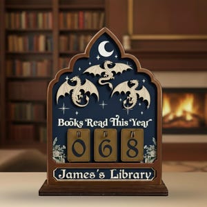 May include: Wooden book tracker with a dark blue background, featuring three dragon silhouettes and the text "Books Read This Year." The counter displays "068." The bottom reads "James's Library."