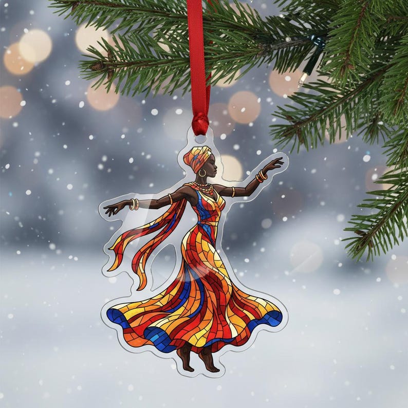 May include: A clear acrylic Christmas decoration depicting a woman in a vibrant dress and headscarf. The ornament is suspended by a red ribbon. The dress is a mosaic of red, orange, yellow, and blue, creating a stained-glass effect.
