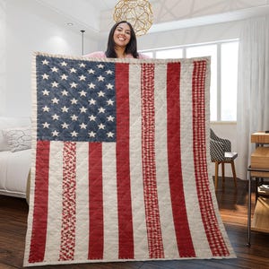 May include: A rectangular quilted throw blanket featuring a design inspired by the American flag. The blue canton contains white stars, while the stripes alternate between solid cream and various red patterns, including floral and gingham prints.