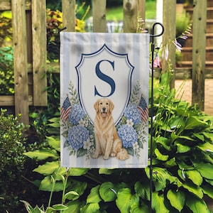 May include: A garden flag with a golden retriever, the letter "S", and blue hydrangeas. The flag has a blue and white striped background with a shield design. Small American flags are on either side of the dog.